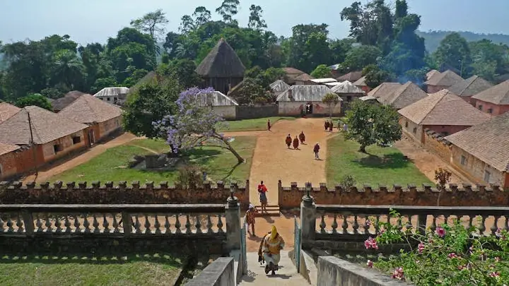 A wide courtyard seen from a balustrade above, a flowering tree at its centre and people crossing the open ground.