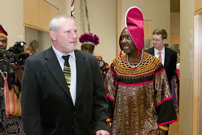 A group in Bafut dress and in suits standing together in a gallery hung with artwork.