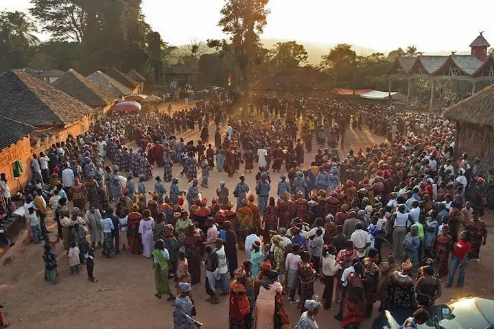 A large crowd filling an open courtyard in low evening light, tiled roofs on every side.